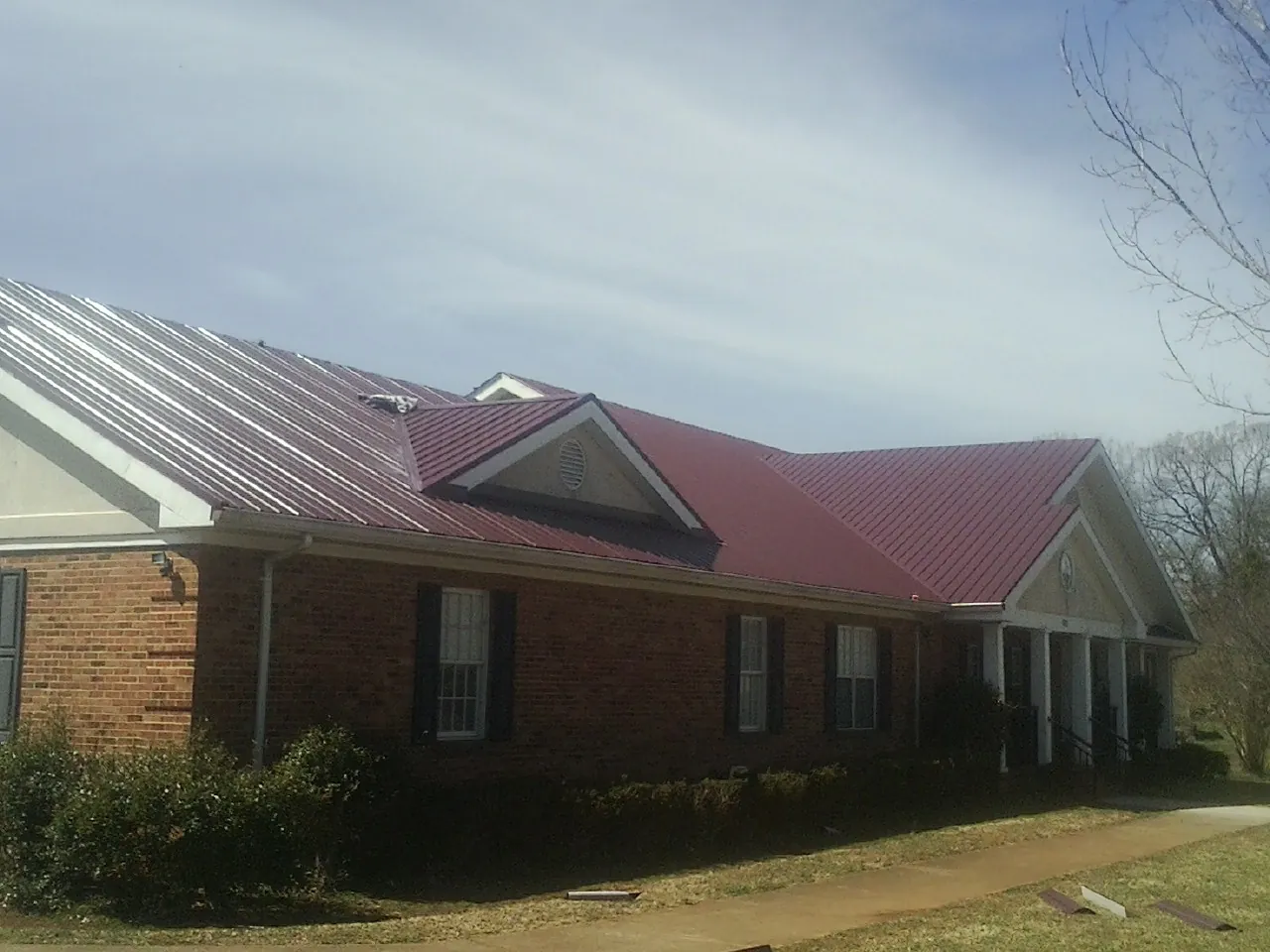 Red metal roof with gabled entries on a long brick building, from a Hail Damage Roof Repair job in Brookville