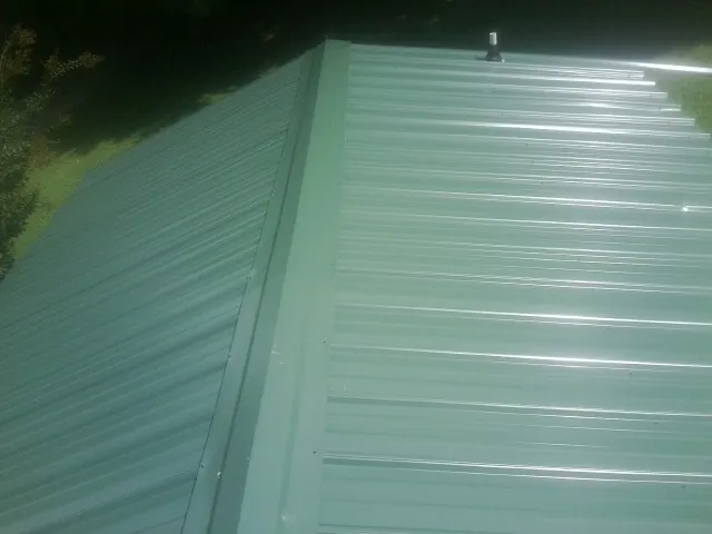 New green metal panels meeting at the ridge of a roof — Flat Roof Repair work by our crew in Brookville