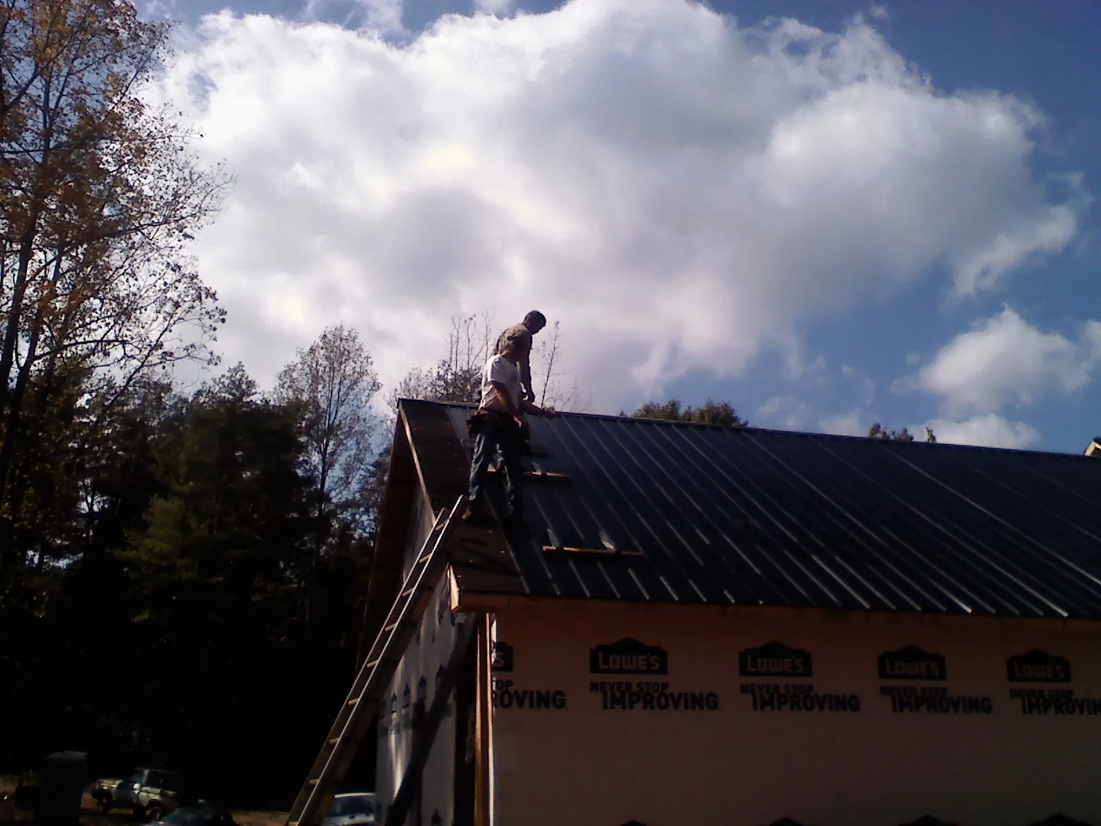 Roofer fastening dark metal panels high against a cloudy sky, from a Roof Inspection job in Brookville